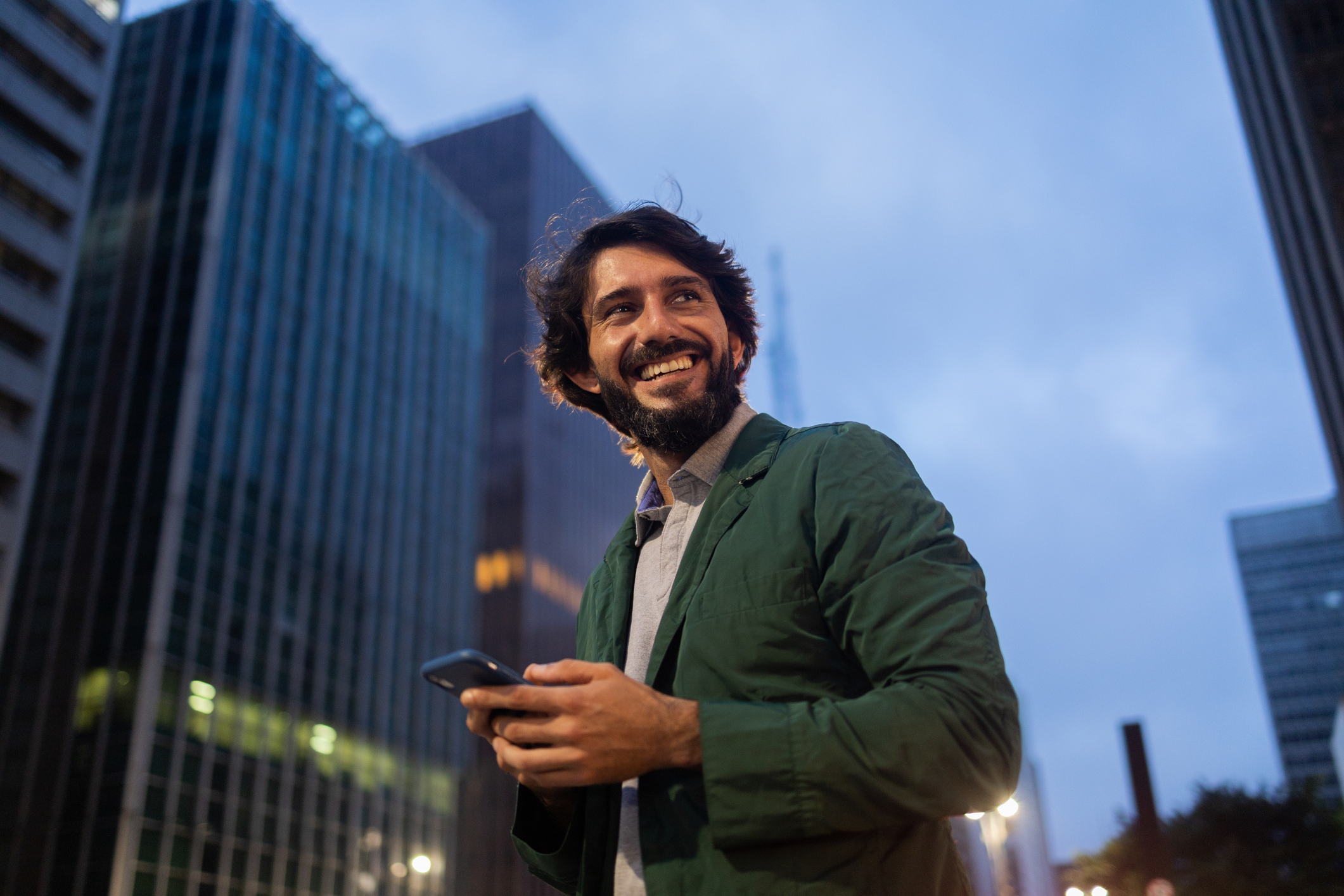 Vista de un joven usando un teléfono inteligente por la noche con el paisaje de la vista de la ciudad en el fondo. Foto de alta calidad - Foto de stock de Hombres libre de derechos