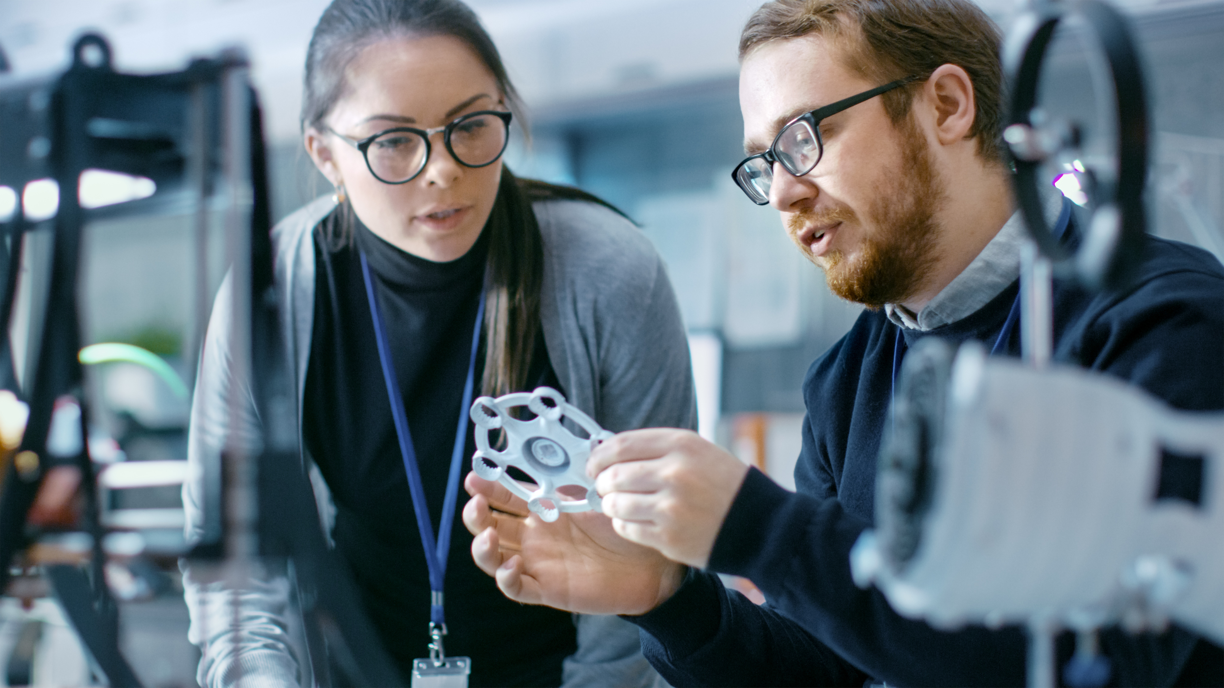 Jóvenes talentosos ingenieros masculinos y femeninos en un laboratorio moderno discutiendo prototipo construido con la ayuda de la impresora 3D. - Foto de stock de Impresión en 3D libre de derechos