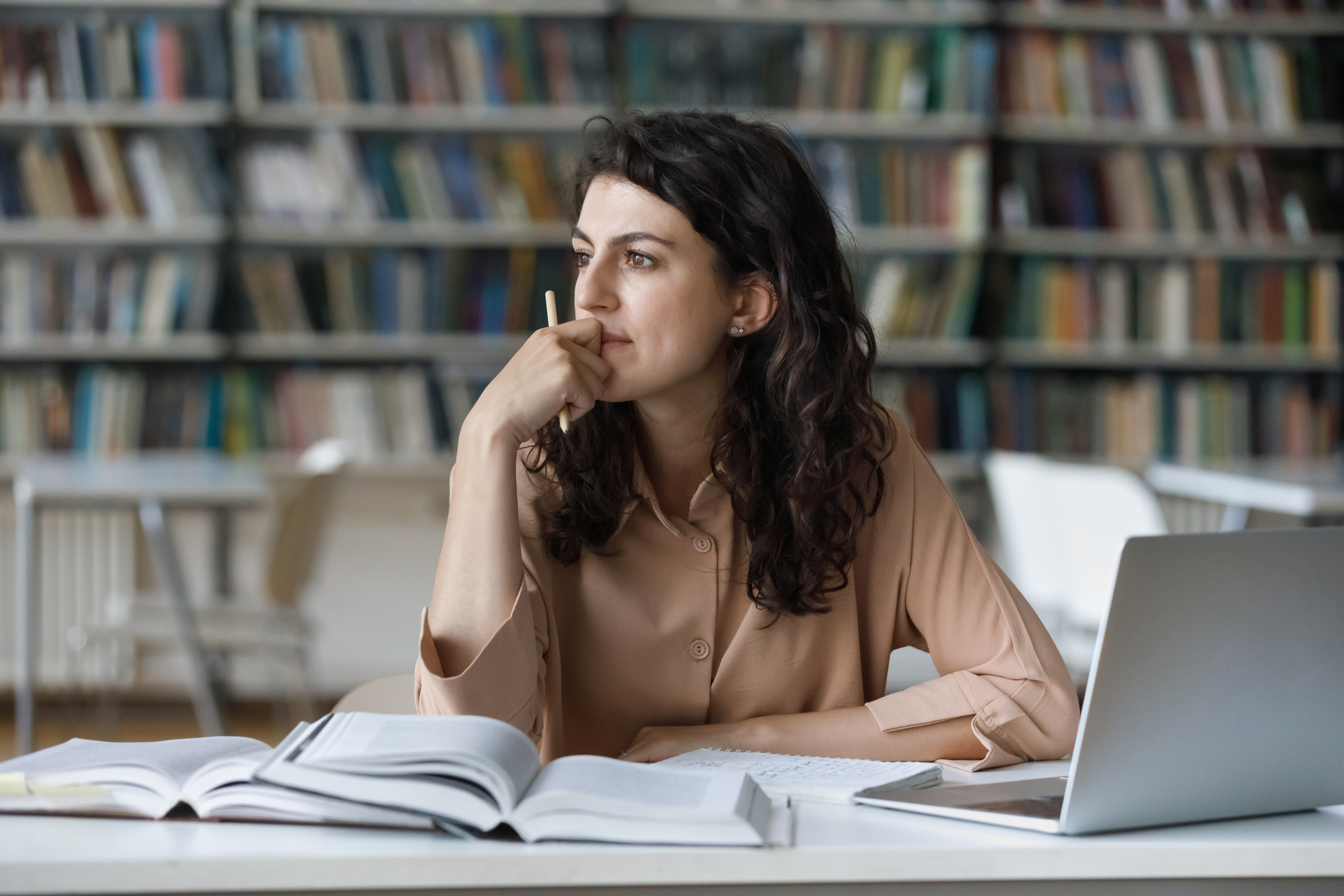 Chica reflexiva que estudia en la biblioteca sentada a la mesa con libros de texto - Foto de stock de Contemplación libre de derechos